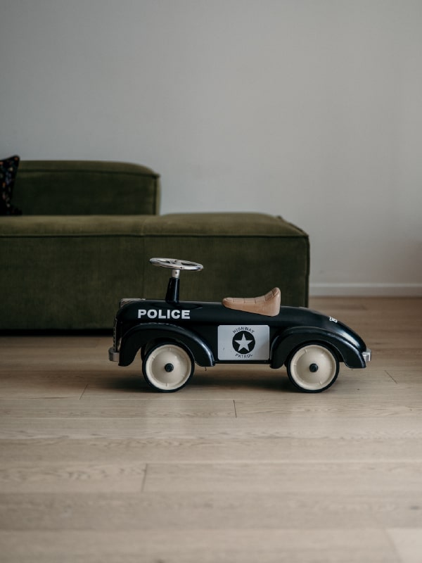 Kleines schwarzes Spielzeug-Polizeiauto steht auf Holzfußboden vor einem grünen Sofa.