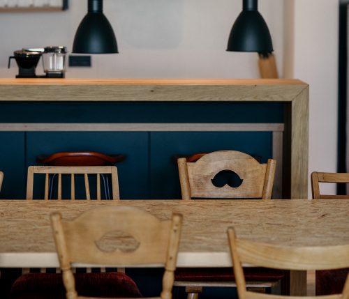 Rustikaler Essbereich mit geschnitzten Holzstühlen, großem Holztisch und moderner Küchenzeile im Hintergrund.